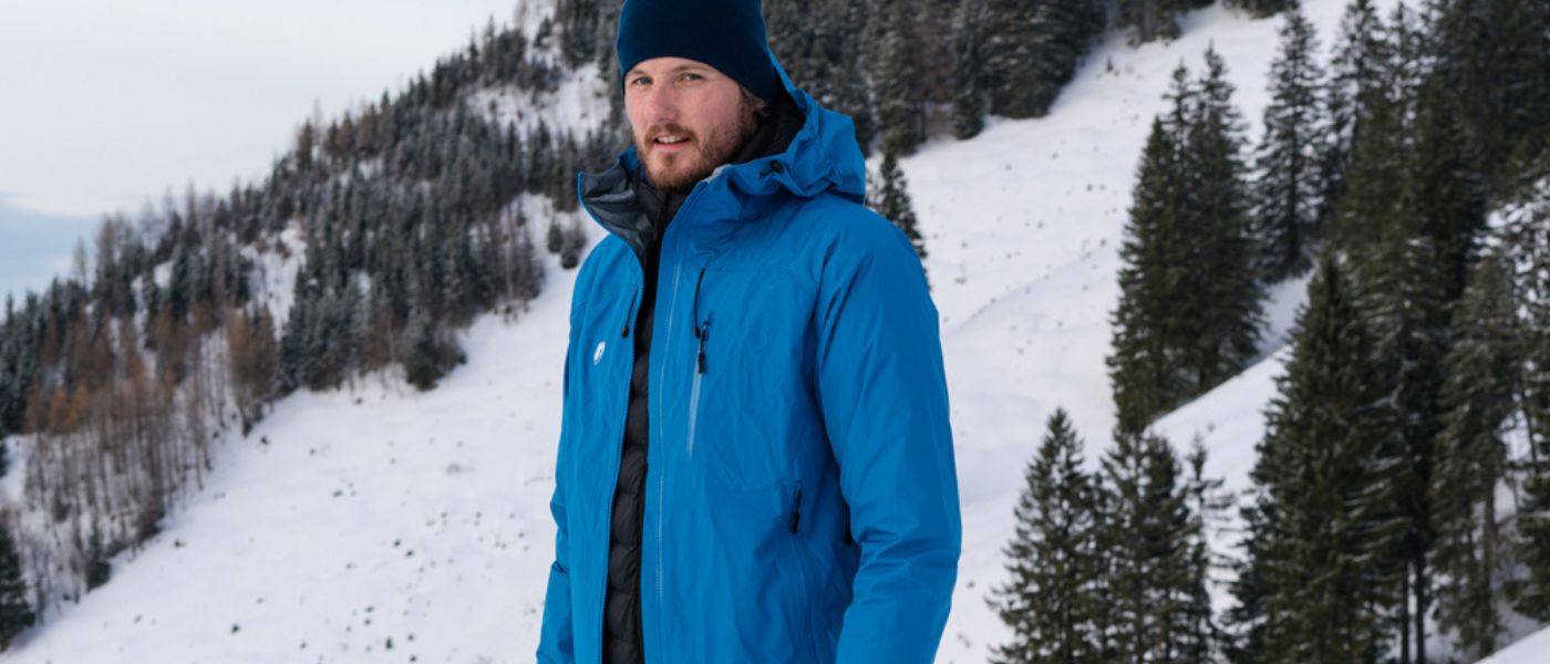Ein Mann in einer blauen Jacke steht im Schnee, passend für Outdoor-Aktivitäten, wie sie auf alpinloakor.shop angeboten werden.