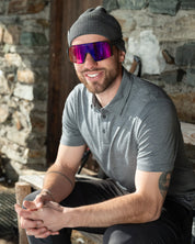 Model sitzt vor Hütte in grauem Merino Coolmax Polo Shirt - perfekt für Outdoor Aktivitäten