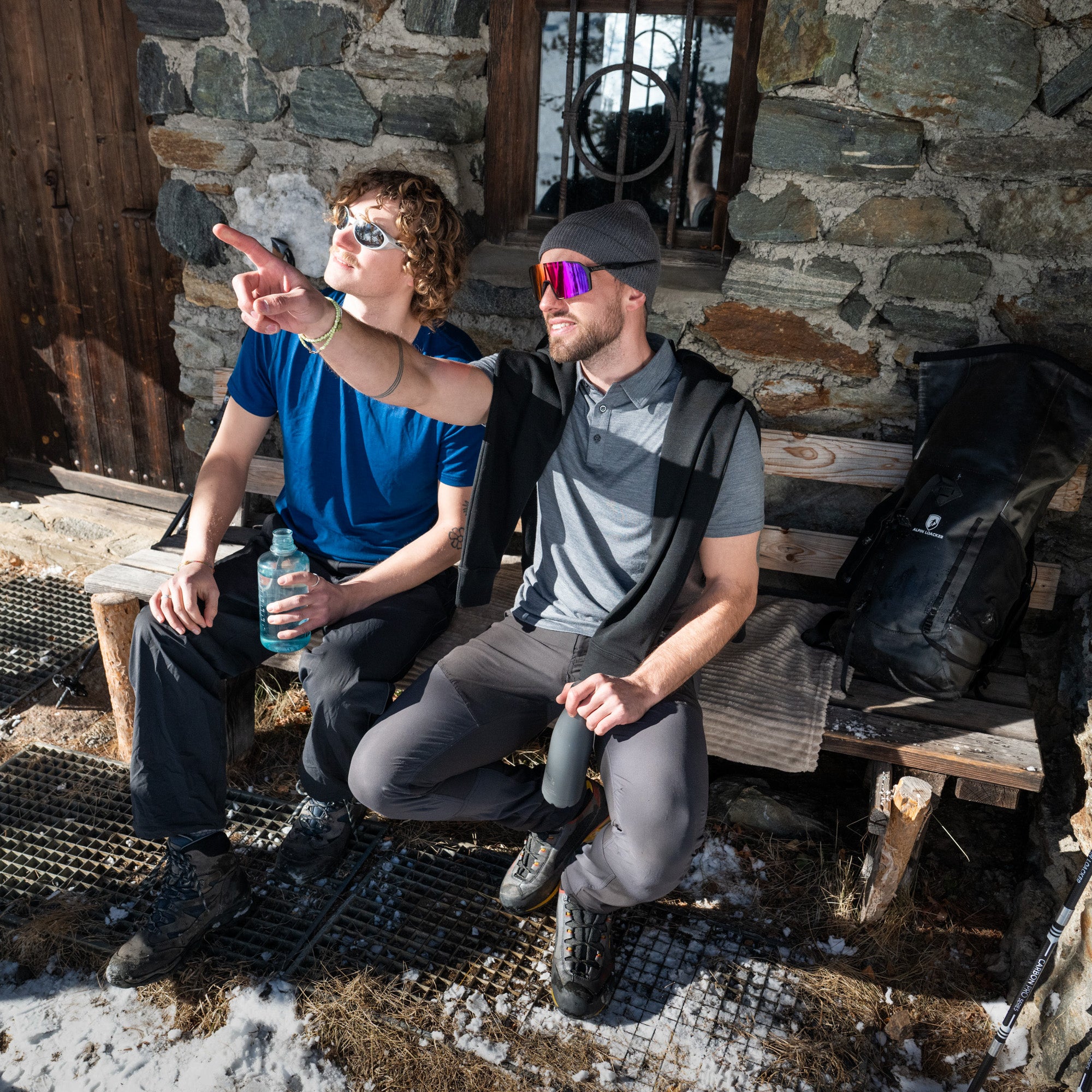Zwei Wanderer sitzen auf einer Bank, der rechte trägt das Merino Coolmax Polo von Alpin Loacker - ideal für Outdoor Aktivitäten