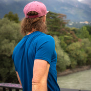 Person mit blauem Merino Coolmax T-Shirt Herren 150 g/m2 von hinten an Flussufer, ideal für Outdoor-Aktivitäten dank Temperaturregulierung und schnelltrocknendem Komfort.