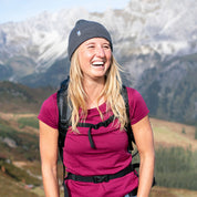 Junge Frau mit Merino Mütze beim Wandern in den Bergen, ideal für Outdoor-Abenteuer. Hergestellt aus 100% Merinowolle für Komfort und Funktionalität.