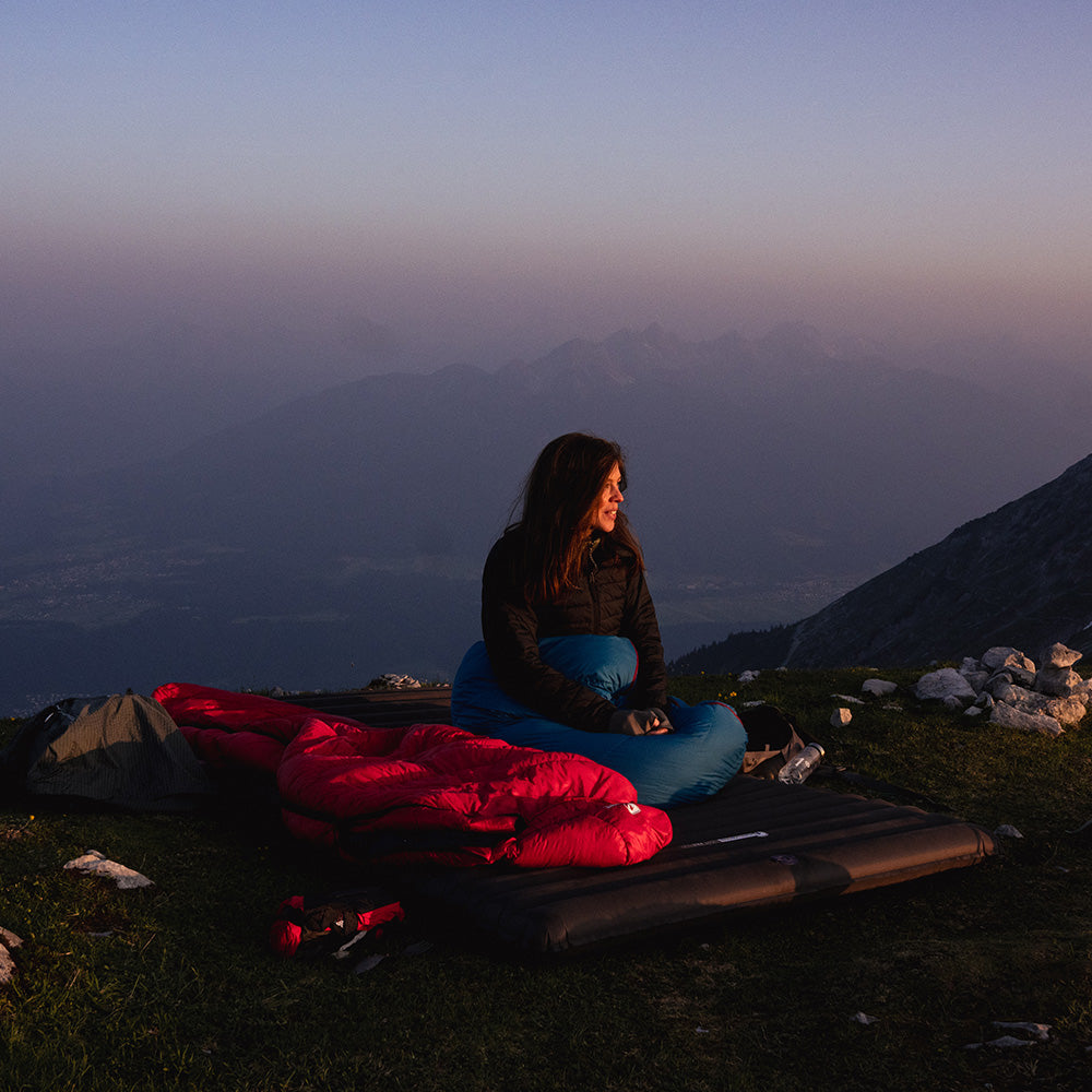 Person auf Berg, sitzt auf Alpin Loacker AIR PAD DOUBLE, einer leichten Isomatte für zwei Personen, ideal für Outdoor-Abenteuer.