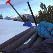 Leichte Isomatte isoliert mit Kunstdaune für 2 Personen auf Schnee, neben einem Schlafsack und Schneewerkzeugen, ideal für Campingabenteuer.