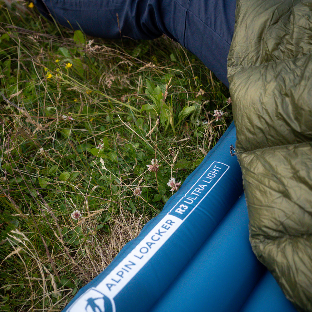 Ultra Leichte Isomatte für 3 Jahreszeiten auf Wiese mit Blumen, teilweise von grünem Schlafsack bedeckt, ideal für Trekking und Camping.