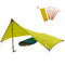 Tarp 500 - das leichte Wingtarp: Aufgebaute Tarp-Shelter mit Trekkingstock, grünem Schlafsack, sechs Alu-Heringen und gelbem Packsack, ideal für Outdoor-Abenteuer.